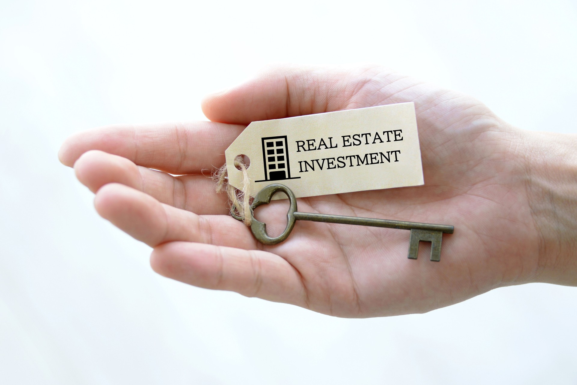 Investor's hand and key with tag "REAL ESTATE INVESTMENT" word written